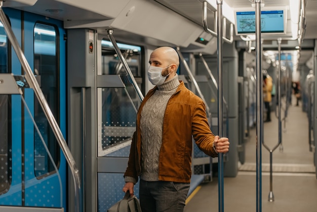 Een man met een baard in een medisch gezichtsmasker om de verspreiding van het coronavirus te voorkomen, rijdt in een moderne metro. Een kale man met een chirurgisch masker houdt sociale afstand in een trein.