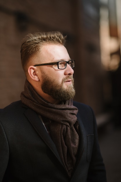 Een man met een baard in een zwarte warme jas met een sjaal poseert om reclame te maken voor herenkleding in de winter. Adverteren voor herenkleding