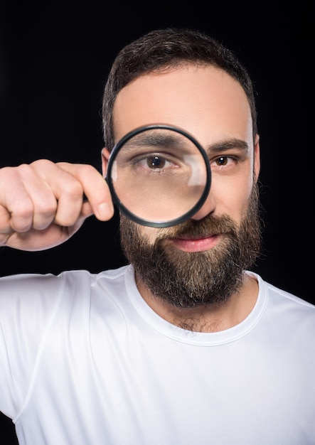 Een man met een baard kijkt door vergrootglas.