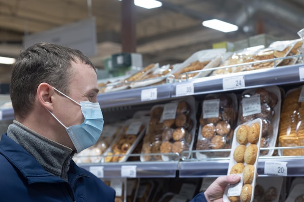 Een man met een beschermend gezichtsmasker kiest eten in een supermarkt Zoet eten Quarantaine