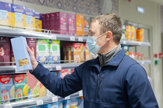 Een man met een beschermend gezichtsmasker kiest producten in de winkel Boodschappen Eten en drinken