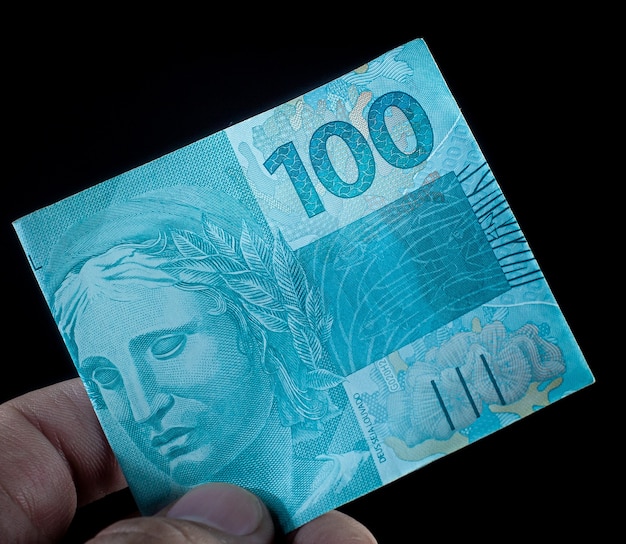een man met een biljet van 100 Braziliaans geld, de Braziliaanse real op zwarte achtergrond