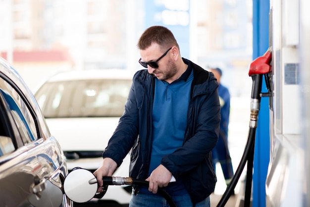 Een man met een blauwe jas en een donkere bril bij een tankstation Hij tankt de auto Petrol Lifestile