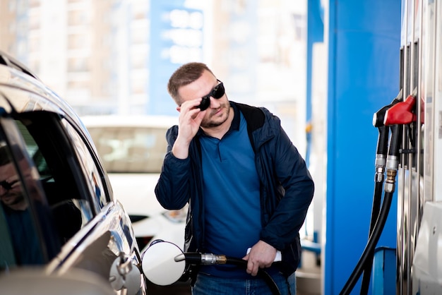 Een man met een blauwe jas en een donkere bril bij een tankstation Hij tankt de auto Petrol Lifestile