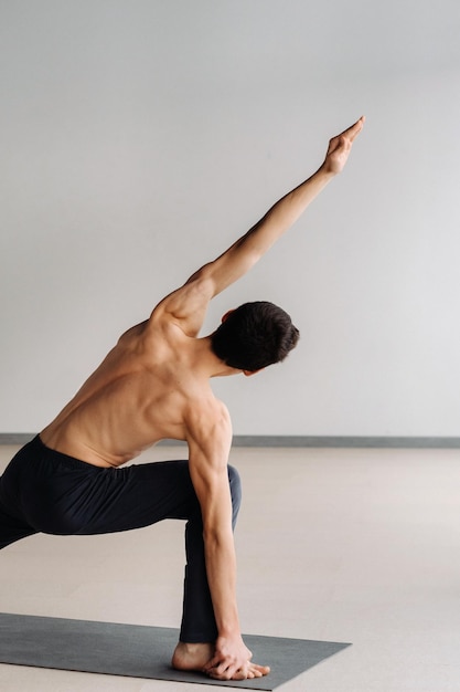 Een man met een blote torso traint staand en doet stretching in de sportschool.