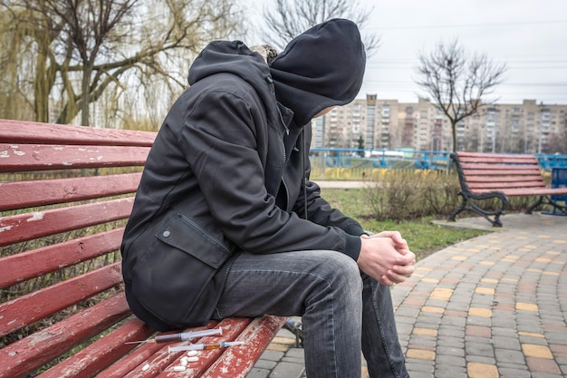 Een man met een capuchon die een drugsverslavingscrisis ervaart, zittend op een bankje
