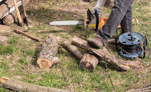 Een man met een elektrische zaag zaagt een boom voor brandhout in de tuin.