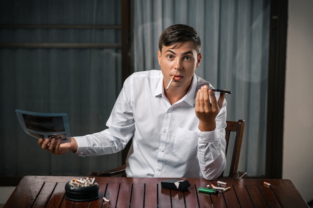 Een man met een foto van een longfoto, zittend aan een tafel met een asbak erop