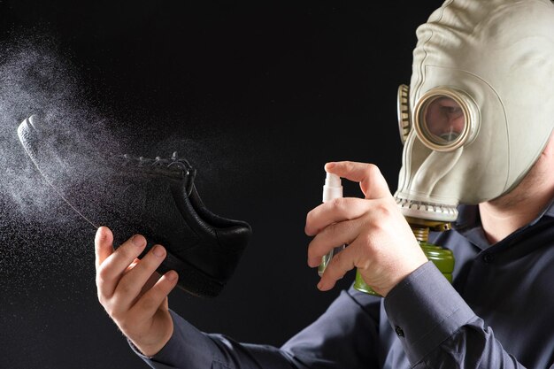 Een man met een gasmasker behandelt zijn schoenen met een geurspray