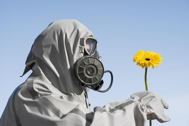 Een man met een gasmasker en een chemisch pak Hij probeert de gele bloem te ruiken Zijaanzicht