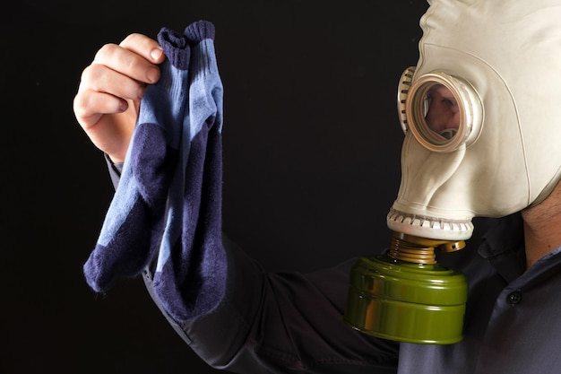 Een man met een gasmasker houdt vieze stinkende sokken vast