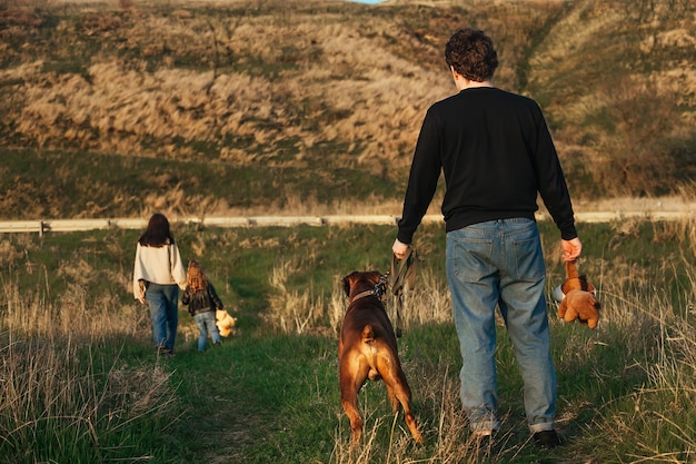 een man met een grote hond en een kinderspeelgoed staat op de weg, zijn vrouw en kind verlaten hem
