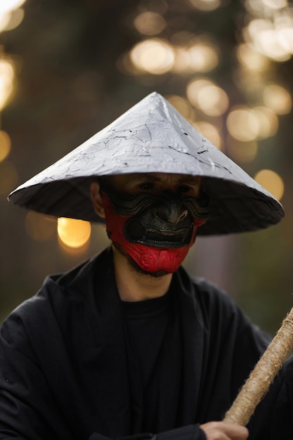 Een man met een hannya-masker, zwarte kimono, zwarte hoed met een bamboestok in handen. Surrealistische samurai, ninja