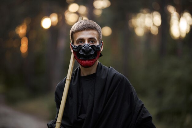 Een man met een hannya-masker, zwarte kimono, zwarte hoed met een bamboestok in handen. Surrealistische samurai, ninja