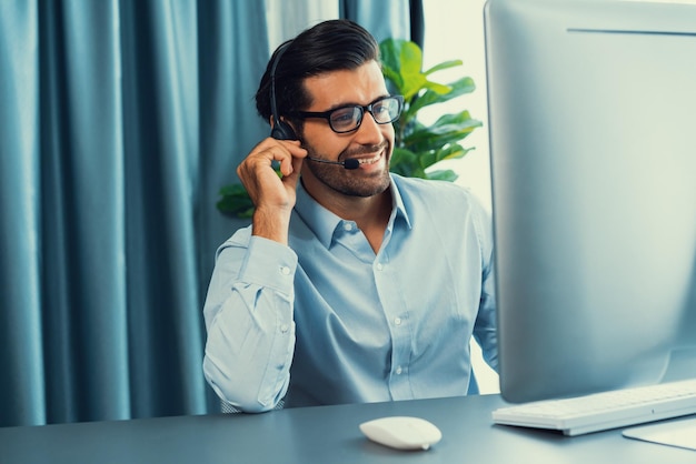 Foto een man met een headset zit aan een bureau met een computer en een monitor waarop callcenter staat.