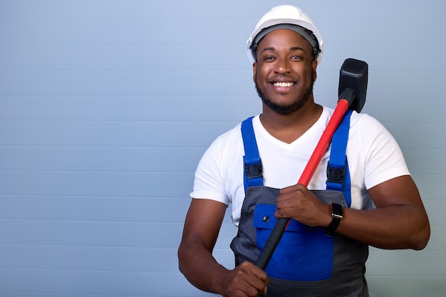 Een man met een helm en werkkleding glimlacht terwijl hij een hamer op zijn schouder houdt