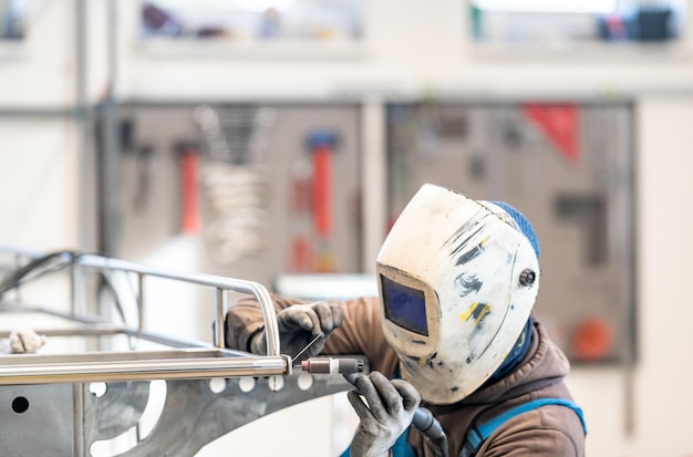 Een man met een helm lasst metaal in een fabriek met behulp van persoonlijke beschermingsmiddelen