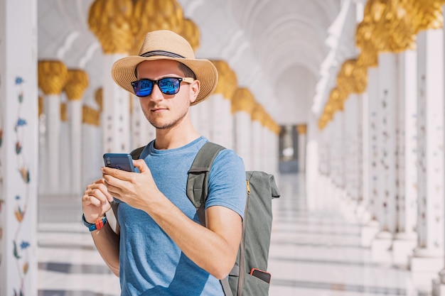 Een man met een hoed en een rugzak gebruikt een mobiele telefoon om een toegangsticket te boeken voor de Grote Moskee van Sheikh Zayed in Abu Dhabi.