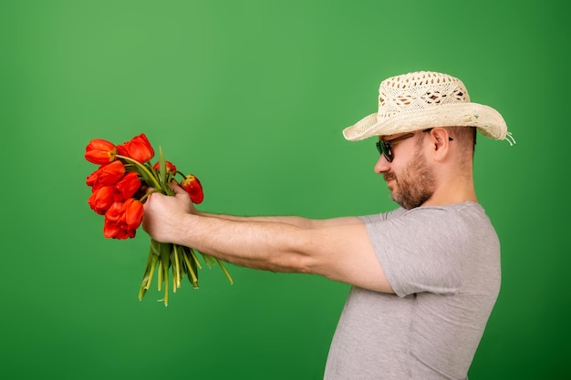 Een man met een hoed en een zonnebril toont een boeket tulpbloemen op een groene achtergrond. Romantiek geeft excuses aan concept