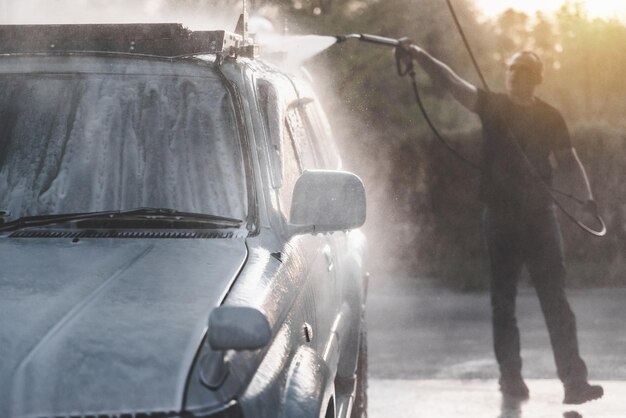 Foto een man met een hogedrukslang wast het schuim af met water bij een zelfbedieningscarwash