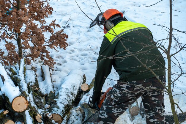 Een man met een kettingzaag zaagt takken en boomstammen Ontbossing in de winter Het werk van een houthakker in strenge winterse omstandigheden Oude bomen omhakken in de stad