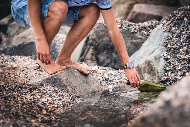 Een man met een klok op zijn hand zet een fles met een boodschap water op de zee