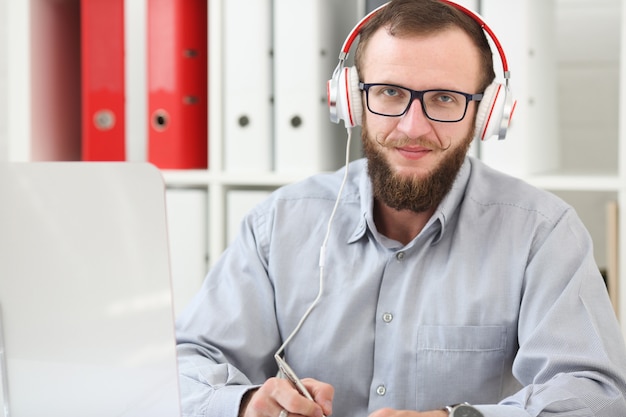 Een man met een koptelefoon luistert naar muziek en leert online. maakt aantekeningen in een notitieboekje en kijkt naar de camera