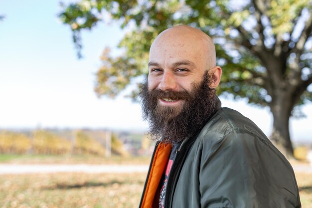 Een man met een lange baard die glimlacht in het zonnige weer hij is kaal en draagt een bom