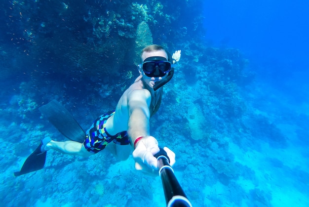 Een man met een masker en snorkel duikt in het blauwe water van de Rode Zee en fotografeert zichzelf