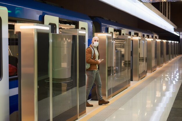 Een man met een medisch gezichtsmasker om de verspreiding van het coronavirus te voorkomen, houdt een smartphone vast bij het verlaten van een moderne metro