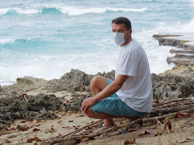 Een man met een medisch masker alleen op het rif strand op zomerdag.