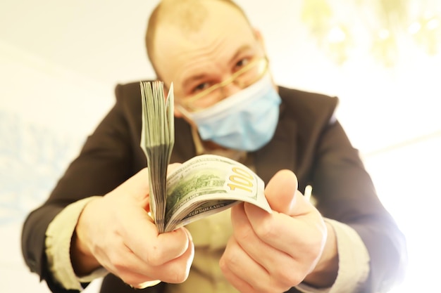 Een man met een medisch masker houdt een pak biljetten van honderd dollar in zijn handen De economische groei