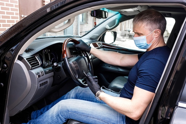 Een man met een medisch wegwerpmasker en handschoenen in een auto met een telefoon in zijn hand