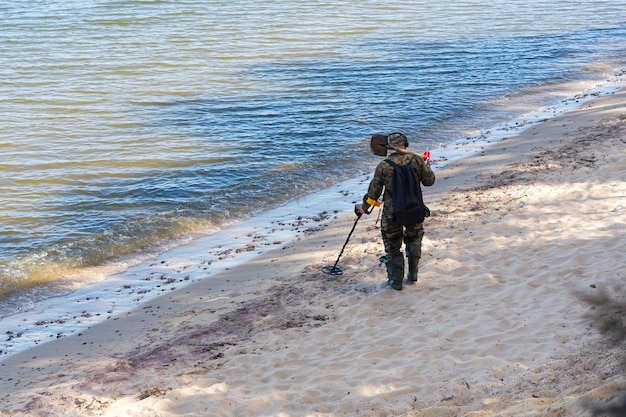 Een man met een metaaldetector loopt langs de waterkant van een zandstrand