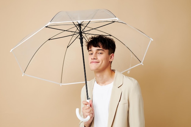 Een man met een open paraplu in een jas die beschermt tegen de regenbeige achtergrond