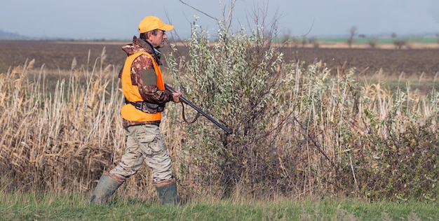 Een man met een pistool in zijn handen en een oranje vest op fazantenjacht in een bosrijke omgeving bij bewolkt weer Jager met honden op zoek naar wild