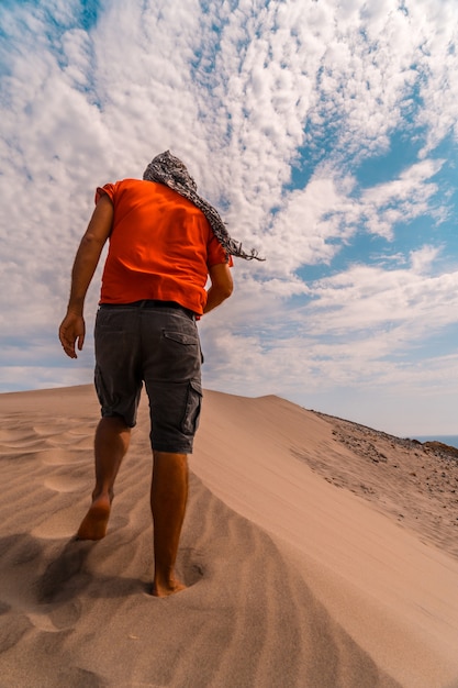 Een man met een rood shirt en een tulband op zijn hoofd, wandelend in de woestijn van de duin