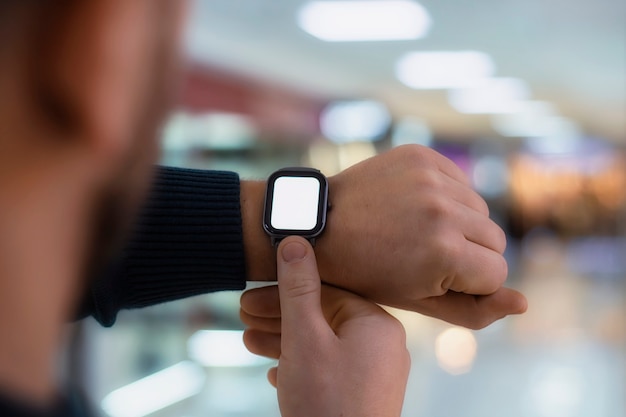 Een man met een smartwatch en een mockup met een wit scherm op zijn hand. Een man gebruikt een fitness-tracker op de achtergrond van een winkelcentrum.