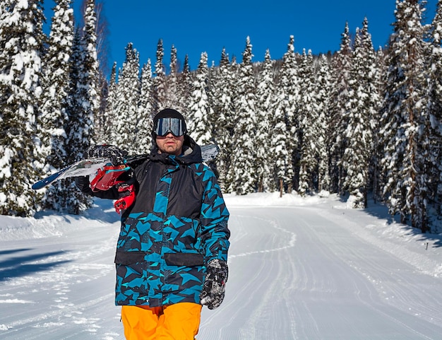 een man met een snowboard loopt over een besneeuwde weg in het bos