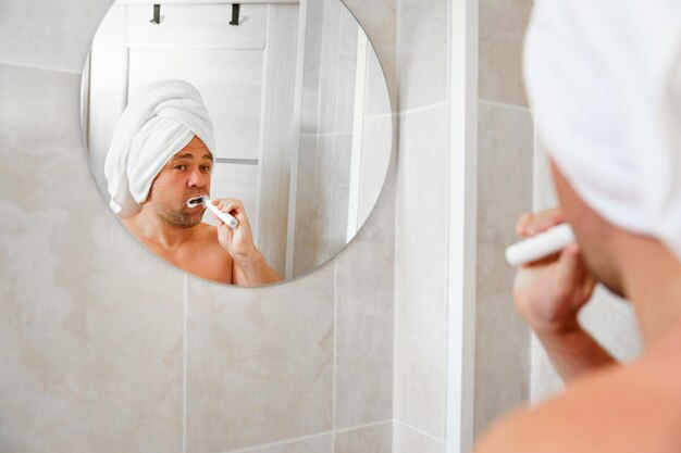 Foto een man met een tulband gemaakt van een handdoek op het hoofd poetst zijn tanden na een ochtenddouche