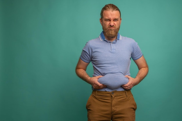 Foto een man met een verdrietig gezicht voelt zijn dikke buik op blauwe achtergrond close-up ruimte voor tekst