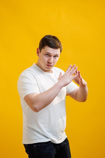 Een man met een wit t-shirt toont het dak van een huis met zijn handen en kijkt naar de camera over de gele studioachtergrond