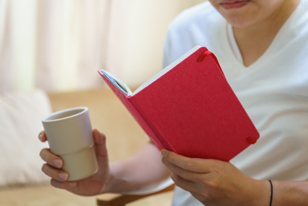 Foto een man met een wit t-shirt zit en leest een boek en houdt een plastic kop warme koffie vast.