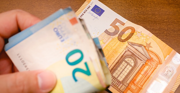 een man met eurobankbiljetten in close-up met vijftig eurobankbiljetten op een houten bureau