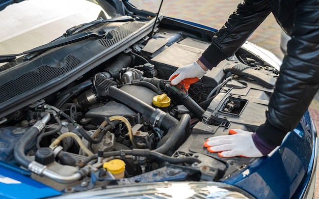 Een man met handschoenen kijkt onder de motorkap van een open auto naar een storing. Concept van eigenaar en autopech