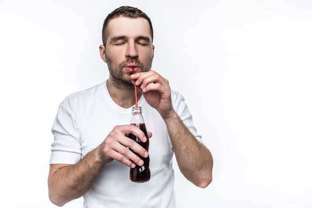 Een man met korte snit drinkt cola uit de fles met een rietje. Deze man eet graag fastfood en drinkt graag zoete drankjes. Geïsoleerd op witte achtergrond