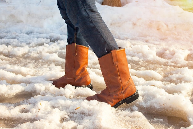 Een man met leren laarzen staat in het vroege voorjaar op plassen. plassen, modder en smeltende sneeuw in rusland. weer en seizoenen. zonsondergang