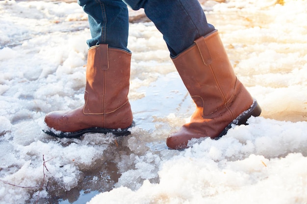 Een man met leren laarzen staat in het vroege voorjaar op plassen. plassen, modder en smeltende sneeuw in rusland. weer en seizoenen. zonsondergang