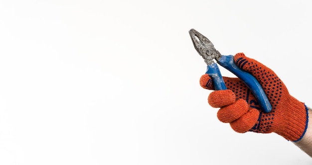 Een man met oranje handschoen houdt een oude tang met blauwe handvatten vast bij een witte muur. Close-up foto