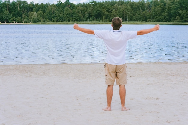 Een man met uitgestrekte handen op de achtergrond van het strand en het bos.